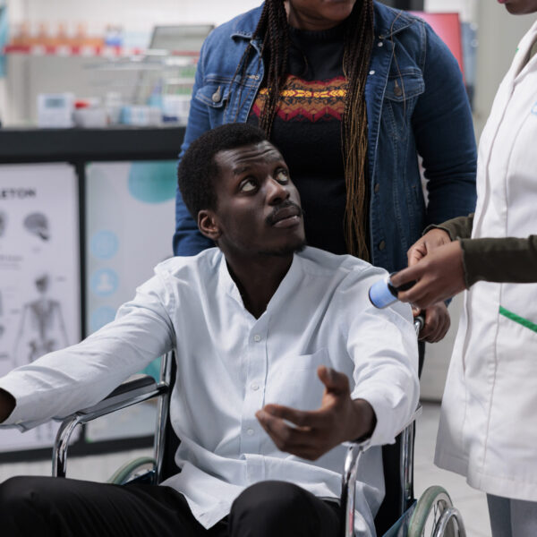 Pharmacy consultant explaining man with disability medications instruction, customer in wheelchair choosing nutritional supplements. Pharmacist recommending medicaments to client